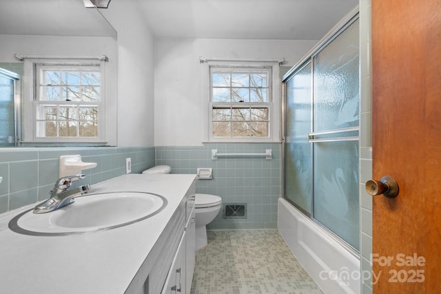 full bathroom with vanity, tile walls, toilet, and combined bath / shower with glass door