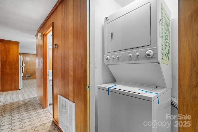 laundry area featuring stacked washer / drying machine and wood walls