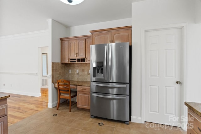 kitchen featuring stainless steel refrigerator with ice dispenser, tasteful backsplash, light tile patterned flooring, light stone countertops, and built in desk