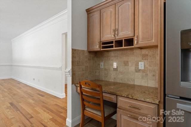 kitchen featuring built in desk, tasteful backsplash, stainless steel fridge with ice dispenser, light stone counters, and crown molding