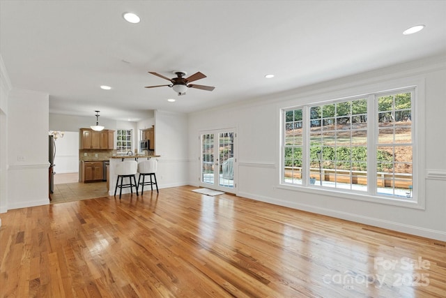 unfurnished living room with ceiling fan, ornamental molding, and light wood-type flooring