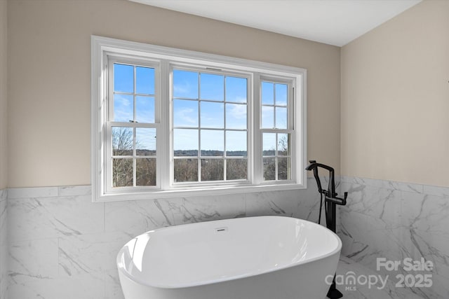 bathroom with a tub to relax in and tile walls