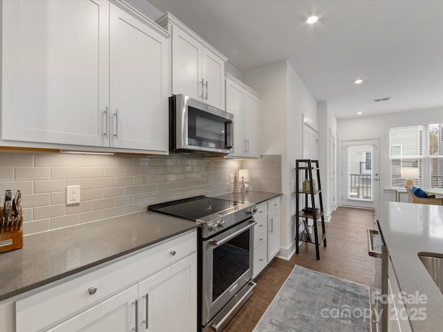 kitchen with dark stone countertops, tasteful backsplash, dark hardwood / wood-style flooring, white cabinetry, and stainless steel appliances