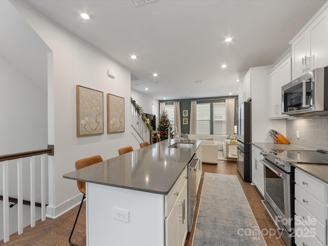 kitchen featuring white cabinetry, sink, stainless steel appliances, a spacious island, and a breakfast bar