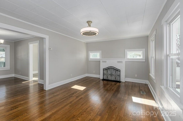 unfurnished living room featuring a healthy amount of sunlight, dark wood-type flooring, and ornamental molding