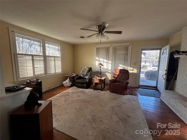 sitting room with visible vents, dark wood finished floors, a ceiling fan, a textured ceiling, and a brick fireplace