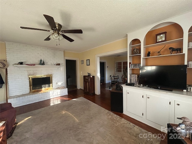 unfurnished living room featuring a textured ceiling, ceiling fan, dark wood-style flooring, ornamental molding, and a brick fireplace