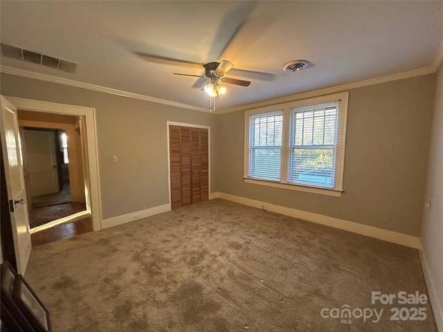 unfurnished bedroom with baseboards, visible vents, dark colored carpet, and ornamental molding