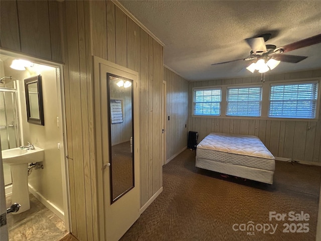 bedroom featuring dark colored carpet, wood walls, a textured ceiling, and ensuite bath