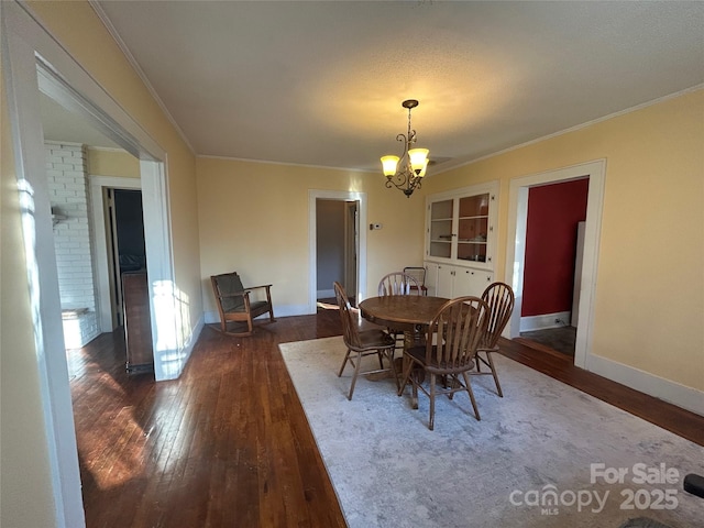 dining area with dark wood-style floors, crown molding, baseboards, and an inviting chandelier