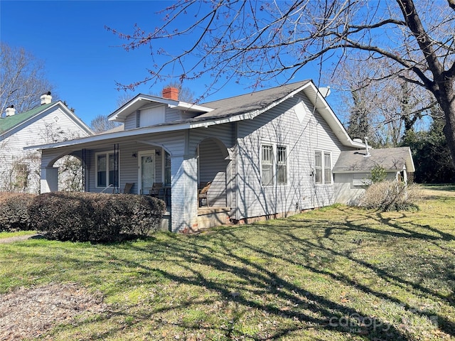 view of side of property featuring covered porch, a yard, and a chimney