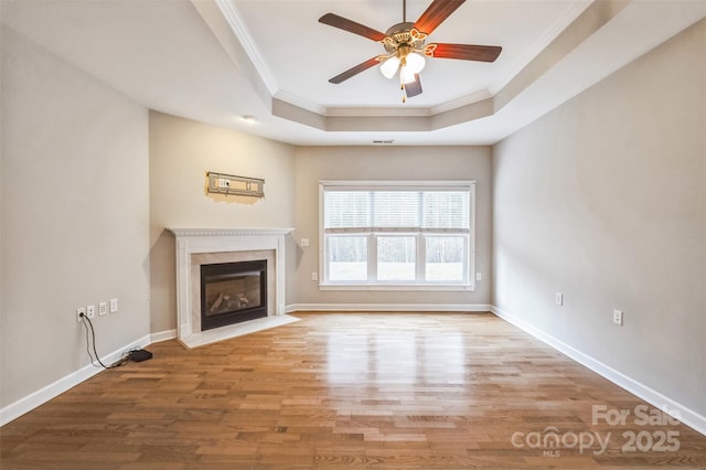 unfurnished living room featuring light wood-type flooring, a raised ceiling, ceiling fan, and crown molding