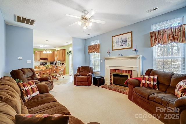 carpeted living room featuring ceiling fan with notable chandelier, a brick fireplace, and a textured ceiling