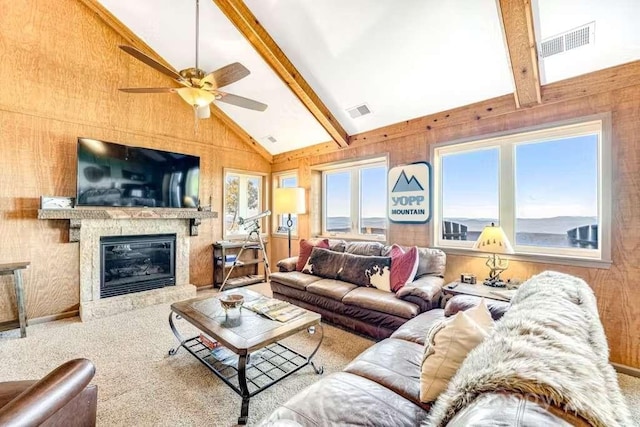 carpeted living room with beamed ceiling, wood walls, and a wealth of natural light