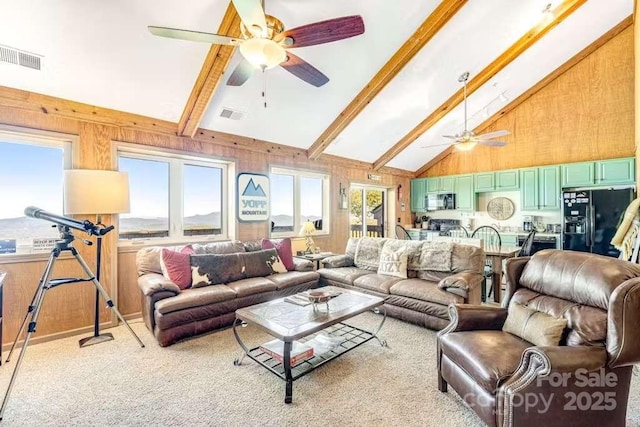 carpeted living room featuring ceiling fan, beamed ceiling, high vaulted ceiling, and wooden walls