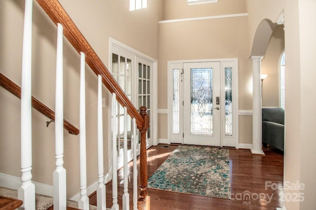 foyer featuring a towering ceiling, dark hardwood / wood-style floors, and decorative columns