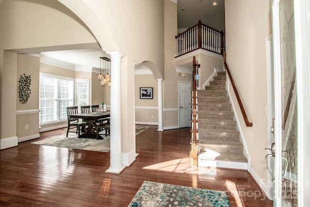 entryway featuring a towering ceiling, dark wood-type flooring, an inviting chandelier, and crown molding