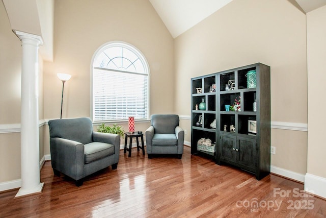 sitting room with high vaulted ceiling, decorative columns, and hardwood / wood-style flooring