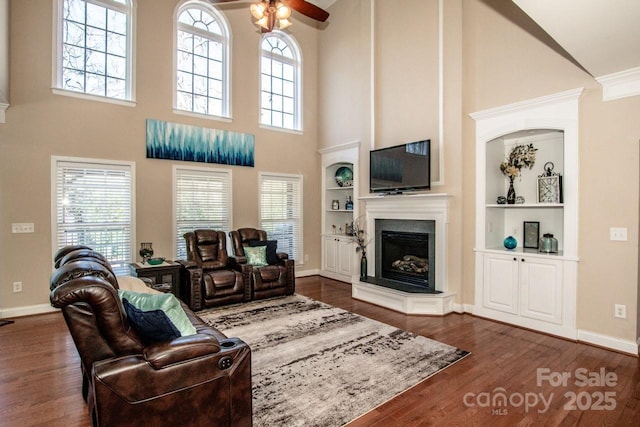 living room featuring ceiling fan, dark hardwood / wood-style flooring, ornamental molding, a high ceiling, and built in shelves