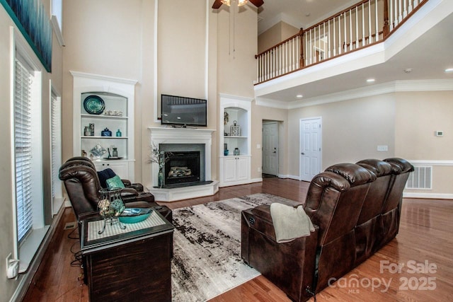 living room featuring a high ceiling, built in shelves, ornamental molding, ceiling fan, and wood-type flooring