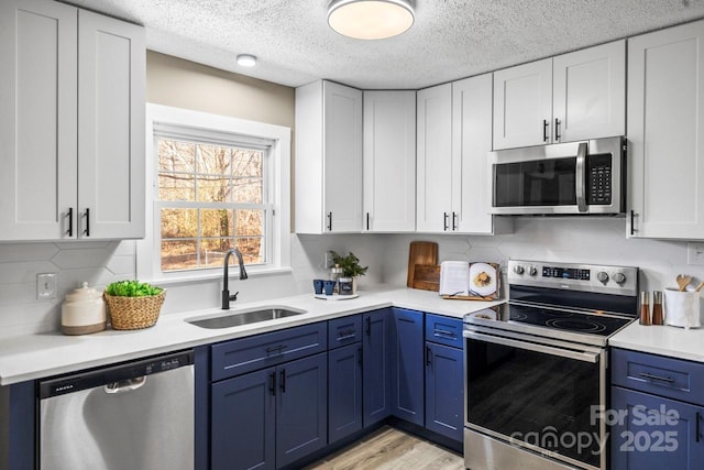 kitchen with white cabinets, appliances with stainless steel finishes, blue cabinetry, and sink