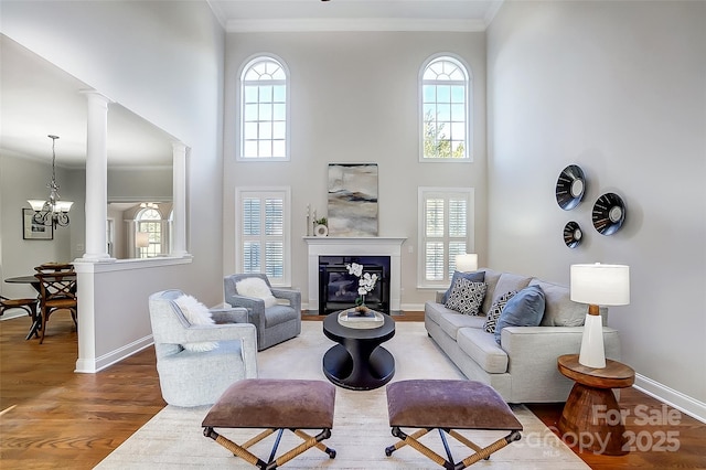 living room with crown molding, wood-type flooring, decorative columns, and a healthy amount of sunlight