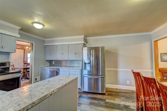 kitchen featuring dark hardwood / wood-style floors, gray cabinets, ornamental molding, tasteful backsplash, and stainless steel appliances