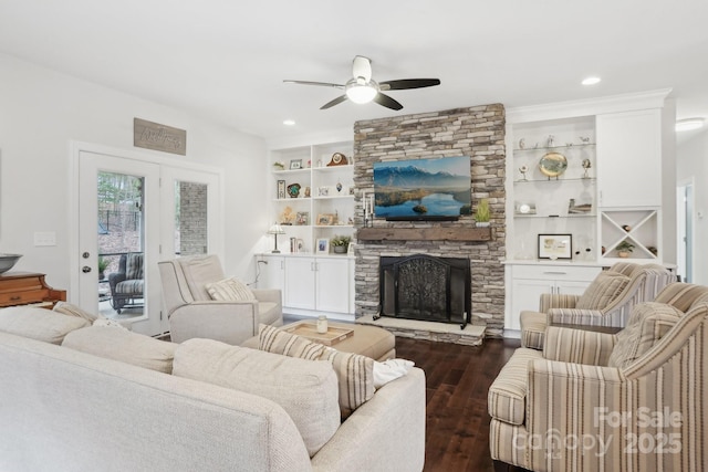 living room with ceiling fan, built in features, dark hardwood / wood-style floors, and a stone fireplace