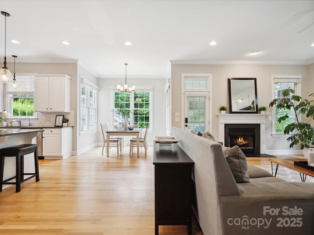 living room with an inviting chandelier, ornamental molding, and light wood-type flooring