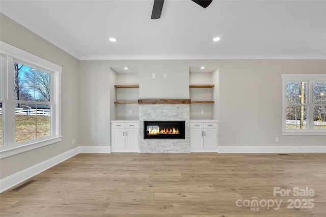 unfurnished living room featuring built in shelves, a fireplace, ornamental molding, and light hardwood / wood-style flooring