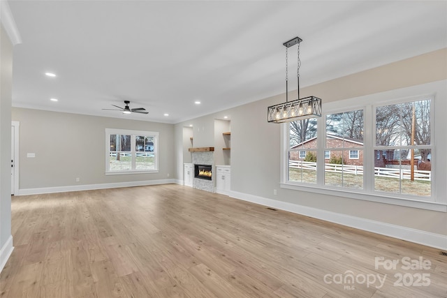 unfurnished living room featuring ceiling fan, plenty of natural light, light hardwood / wood-style flooring, and a stone fireplace