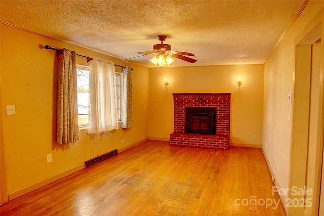 unfurnished living room with wood-type flooring, a brick fireplace, a textured ceiling, and ceiling fan