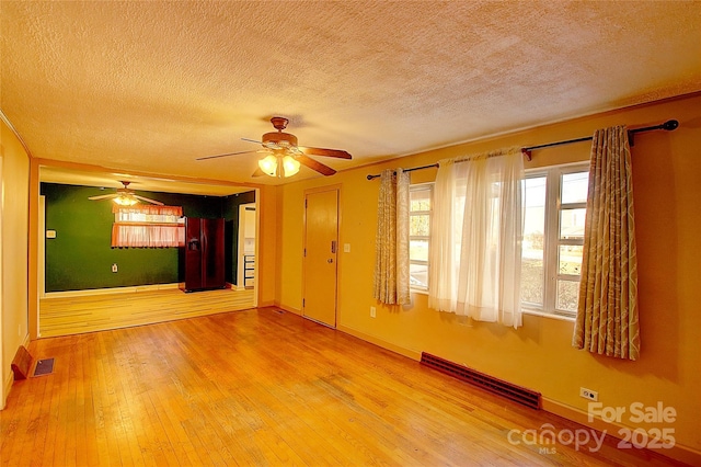 interior space with a baseboard heating unit, a textured ceiling, ceiling fan, and wood-type flooring