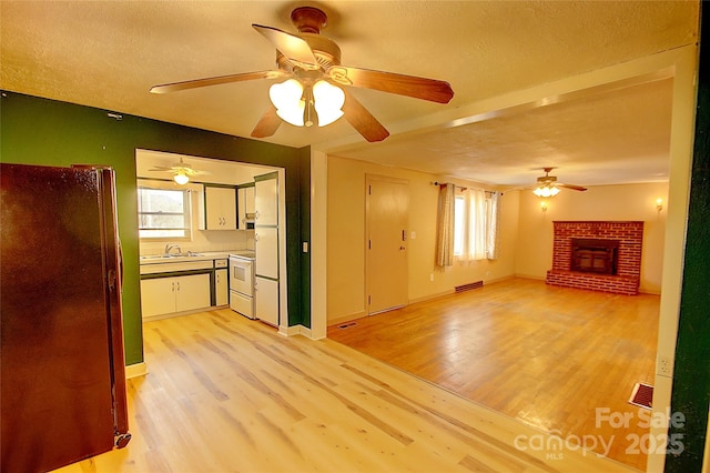 unfurnished living room featuring sink, light wood-type flooring, plenty of natural light, and a fireplace