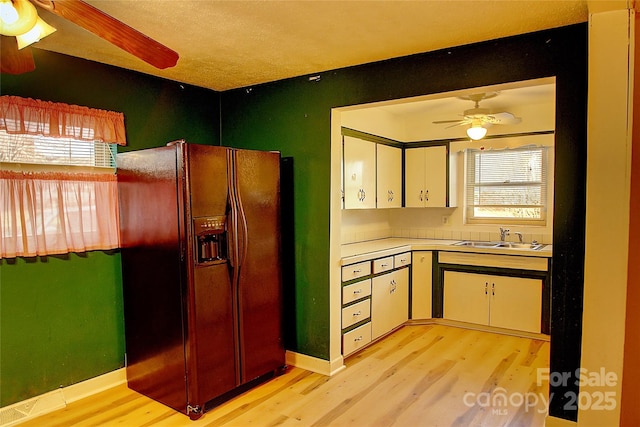 kitchen with black fridge with ice dispenser, light hardwood / wood-style floors, white cabinetry, ceiling fan, and sink