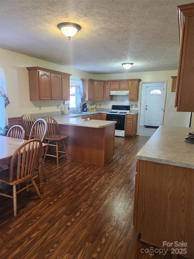 kitchen with gas stove, kitchen peninsula, dark hardwood / wood-style flooring, white refrigerator, and a textured ceiling