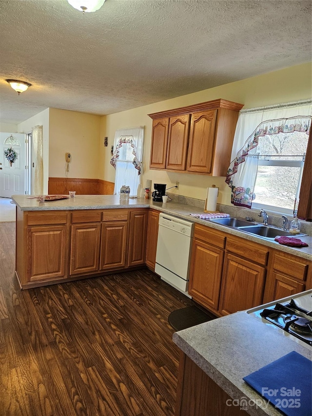 kitchen featuring dark wood-style floors, dishwasher, a peninsula, and a sink