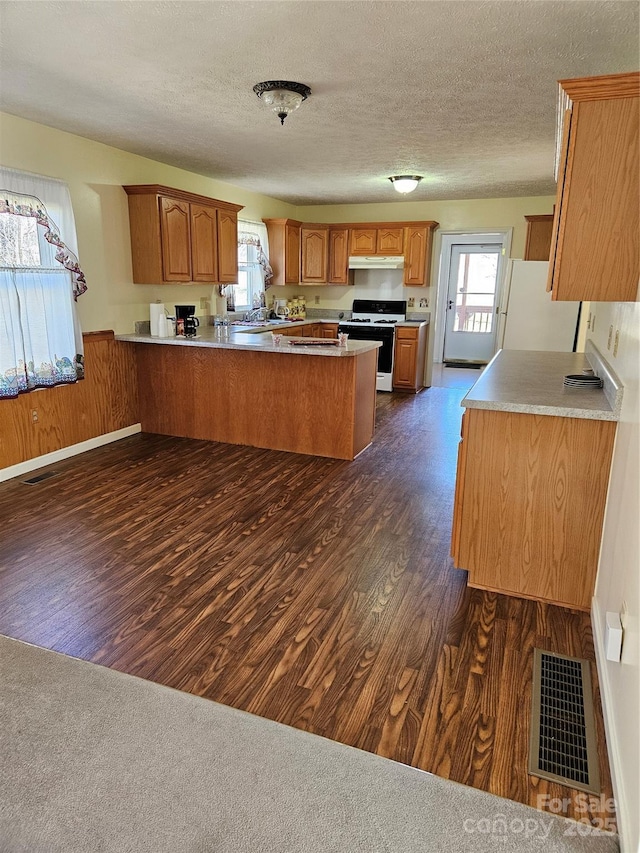 kitchen with white appliances, visible vents, dark wood-style floors, a peninsula, and under cabinet range hood