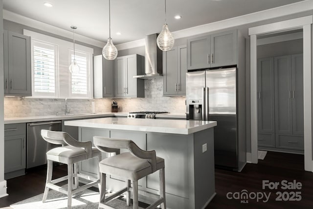 kitchen featuring pendant lighting, a center island, stainless steel appliances, wall chimney range hood, and sink