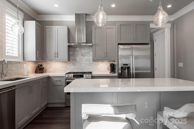 kitchen featuring pendant lighting, stainless steel appliances, wall chimney range hood, gray cabinetry, and sink