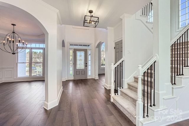 foyer entrance with dark hardwood / wood-style flooring, an inviting chandelier, plenty of natural light, and crown molding