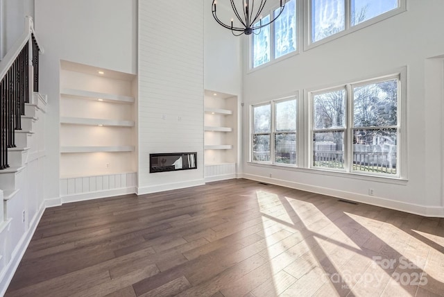 unfurnished living room featuring a high ceiling, a large fireplace, an inviting chandelier, and built in features