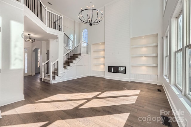 unfurnished living room featuring a fireplace, built in features, a towering ceiling, and a chandelier