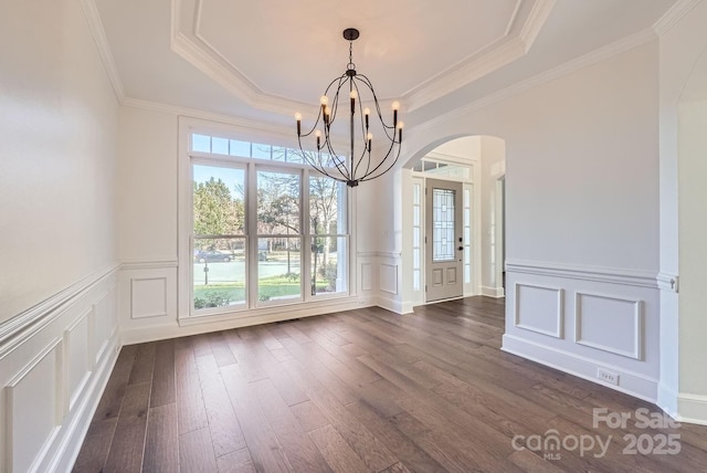 unfurnished dining area featuring a notable chandelier, dark wood-type flooring, crown molding, and a tray ceiling