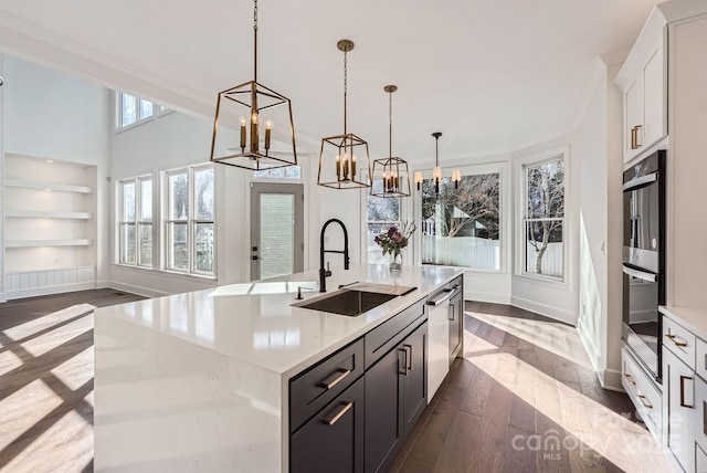 kitchen with sink, decorative light fixtures, built in features, white cabinets, and an island with sink