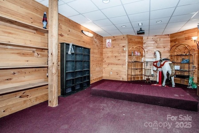 interior space featuring a paneled ceiling, wooden walls, and dark colored carpet