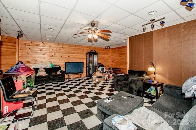 rec room featuring a paneled ceiling, wood walls, and ceiling fan