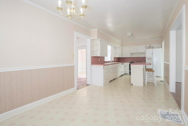 kitchen with white appliances, hanging light fixtures, ornamental molding, a kitchen island, and white cabinetry