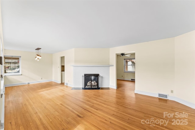 unfurnished living room with ceiling fan with notable chandelier and hardwood / wood-style floors