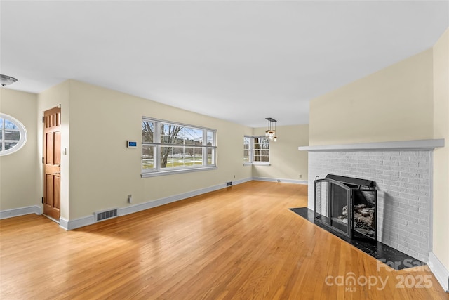 unfurnished living room featuring a brick fireplace, an inviting chandelier, and light hardwood / wood-style flooring